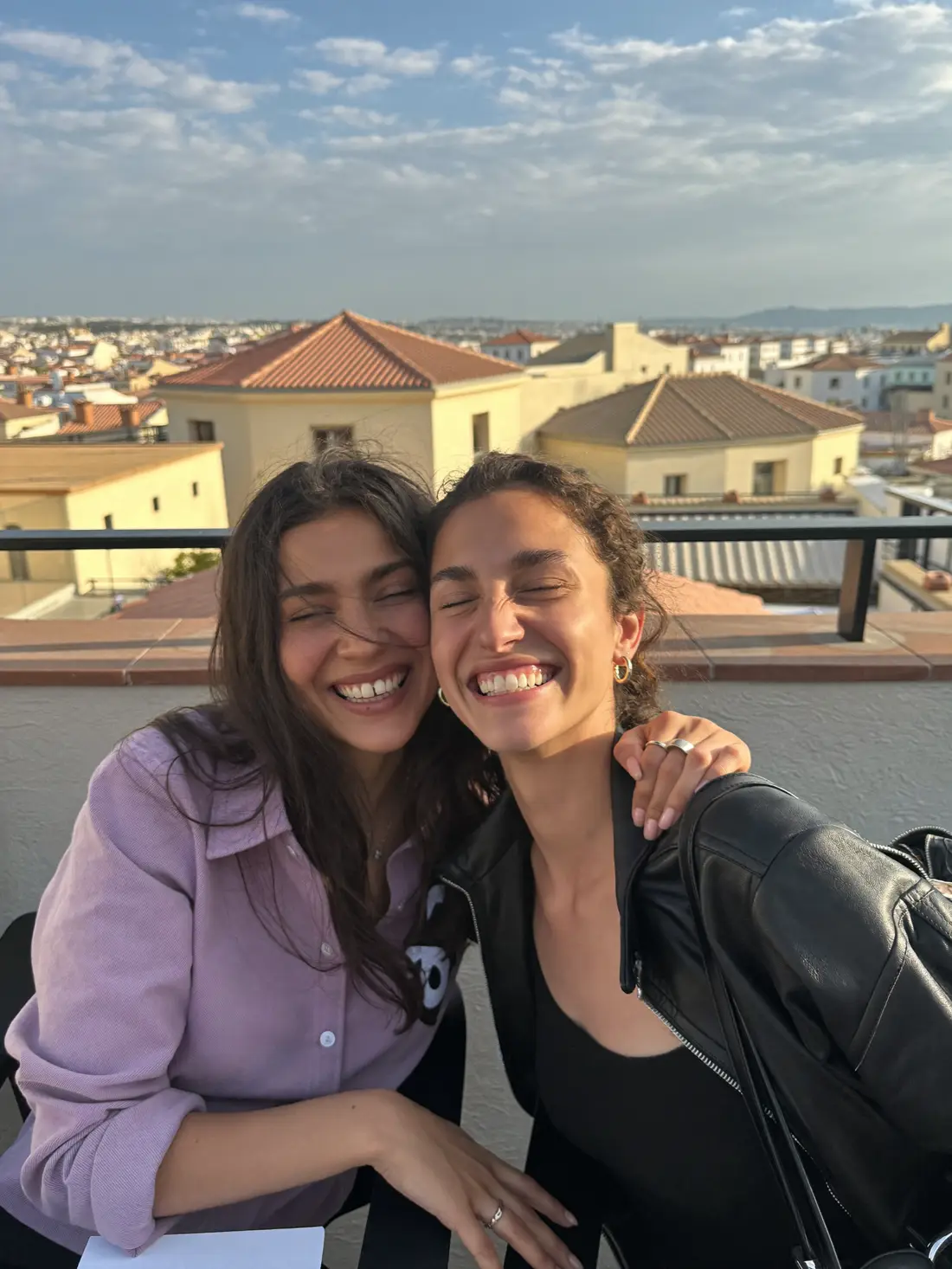 Dos amigas se abrazan riendo en la azotea a la hora dorada